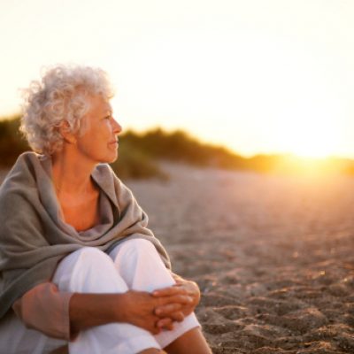 Old woman sitting on the beach looking away