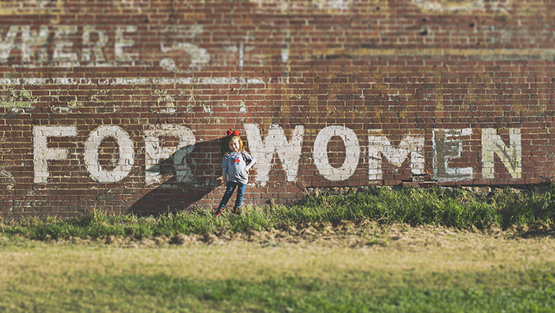girl standing in front of brick wall saying for women