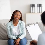 Successful therapy. Young female client having consultation with psychologist, grateful for professional help at clinic. Happy black lady speaking with her psychotherapist, solving emotional problem