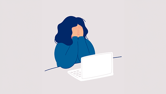 Image of a girl sat at her laptop with hands covering her face like she is sad or crying