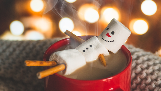 Marshmallow snow-man melts in a mug of hot chocolate.