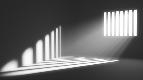 Light shines through prison bars casting a shadow on bleak grey walls.