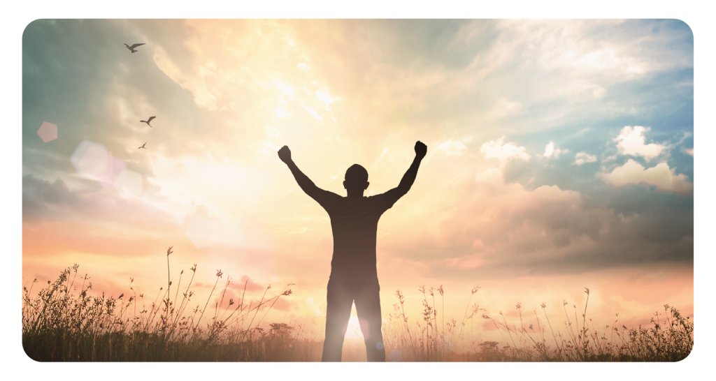 Triumphant person raises arms looking out at a multicolored sunrise.