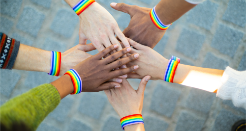 group of people putting their hands together wearing rainbow bracelets